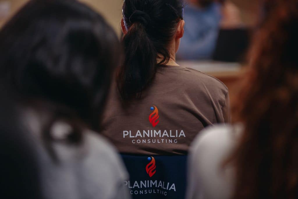 Femme assise, portant un t-shirt marron avec le visuel de "Planimalia consulting", expert en protection animale dans les gestions de crise